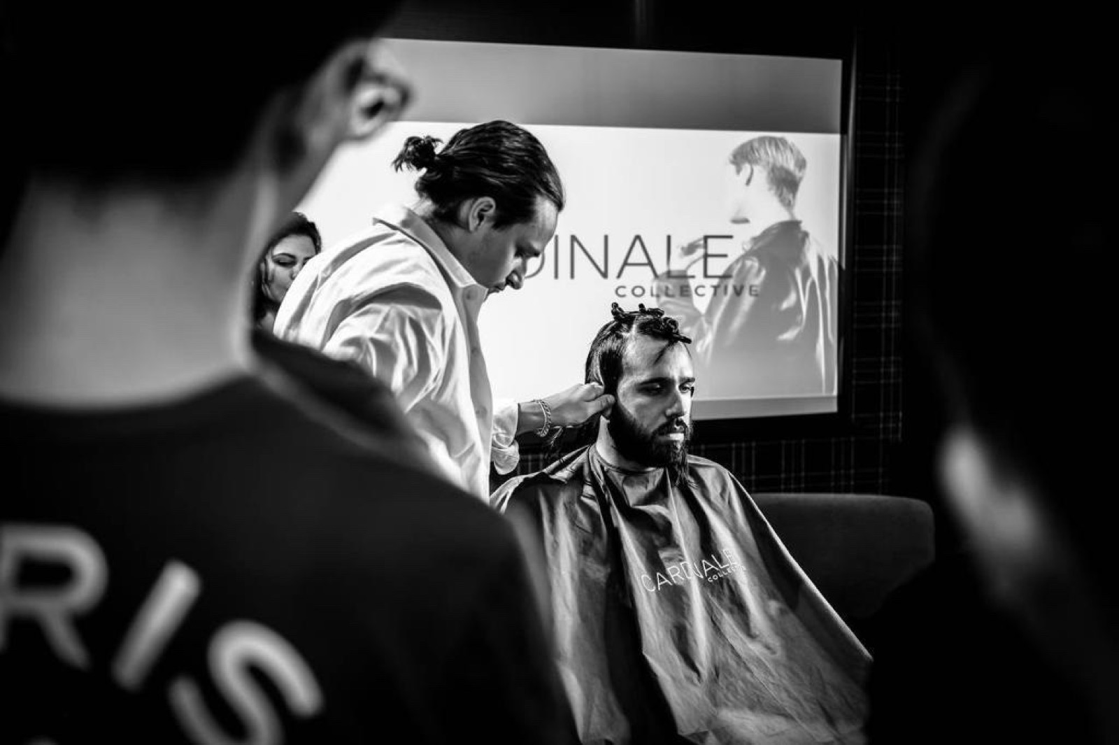 Gianni cutting a model's hair in front of a Cardinale Collective screen while students look on