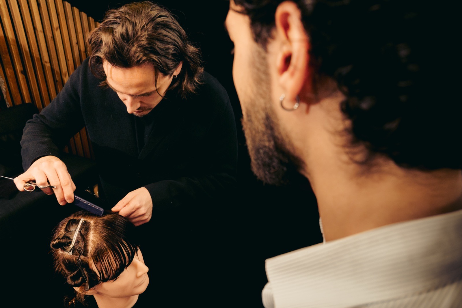 Gianni sectioning hair on a training head as a student looks on