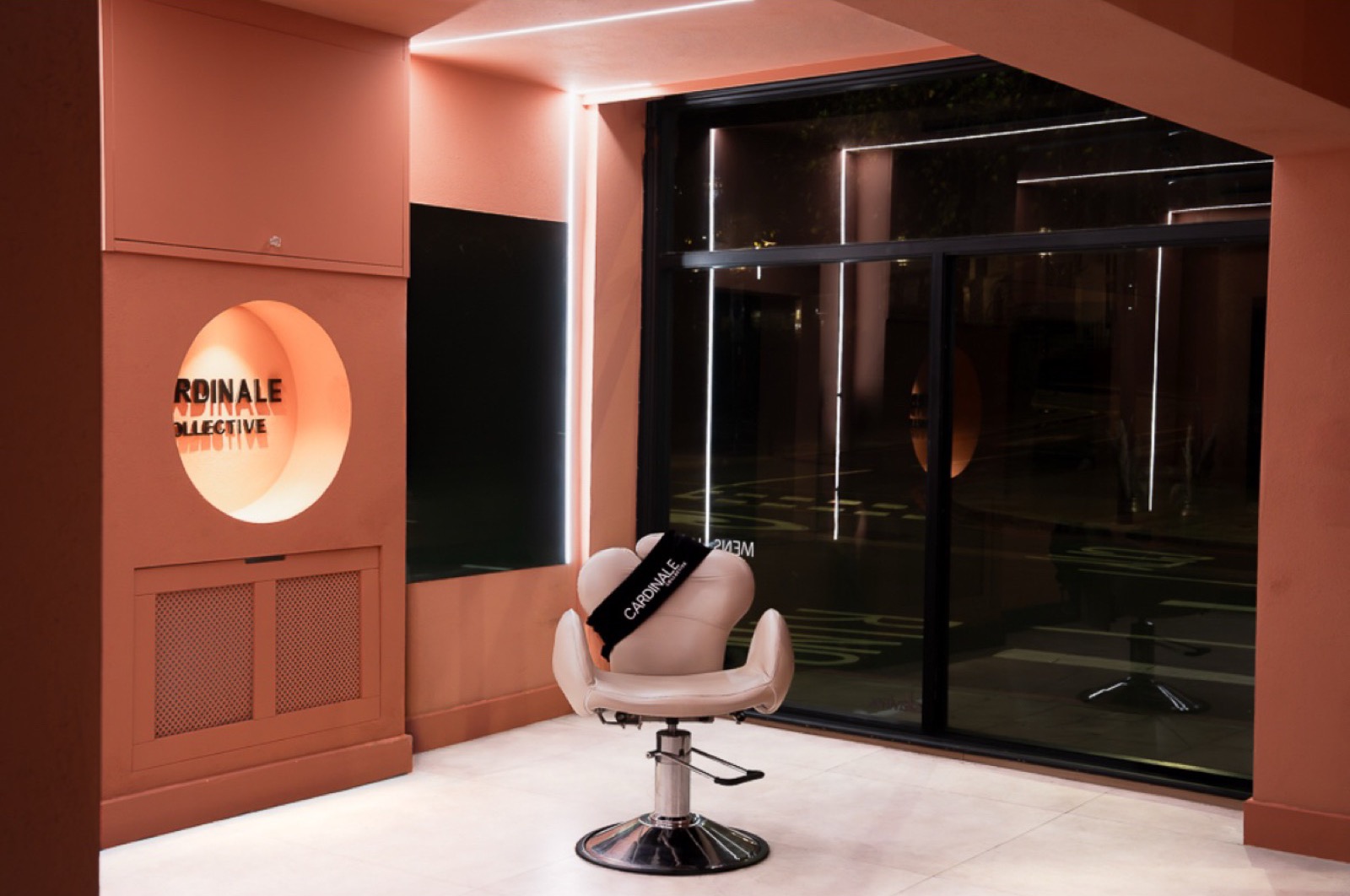 The salon chair in front of the shopfront window, with the Cardinale Collective sign glowing in a round alcove
