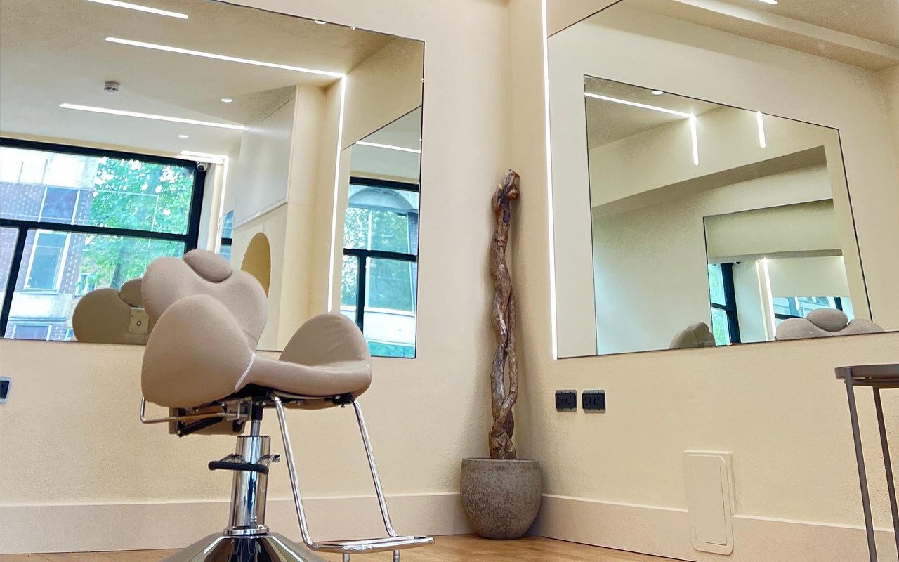 Inside the salon: cream chair, white walls, tall mirrors